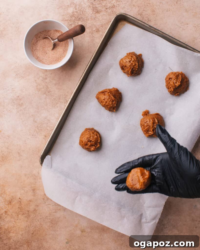 Pillowy Pumpkin Spice Cookies 5 Dampened hands gently shaping pumpkin cookie dough balls on a baking sheet, ensuring a smooth, uniform appearance before baking.