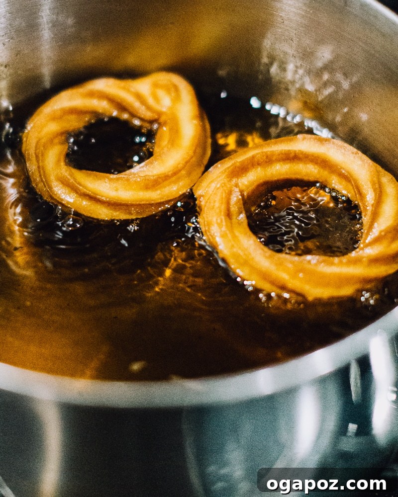 Airy French Delights 14 French Cruller dough being carefully placed into hot oil with tongs.