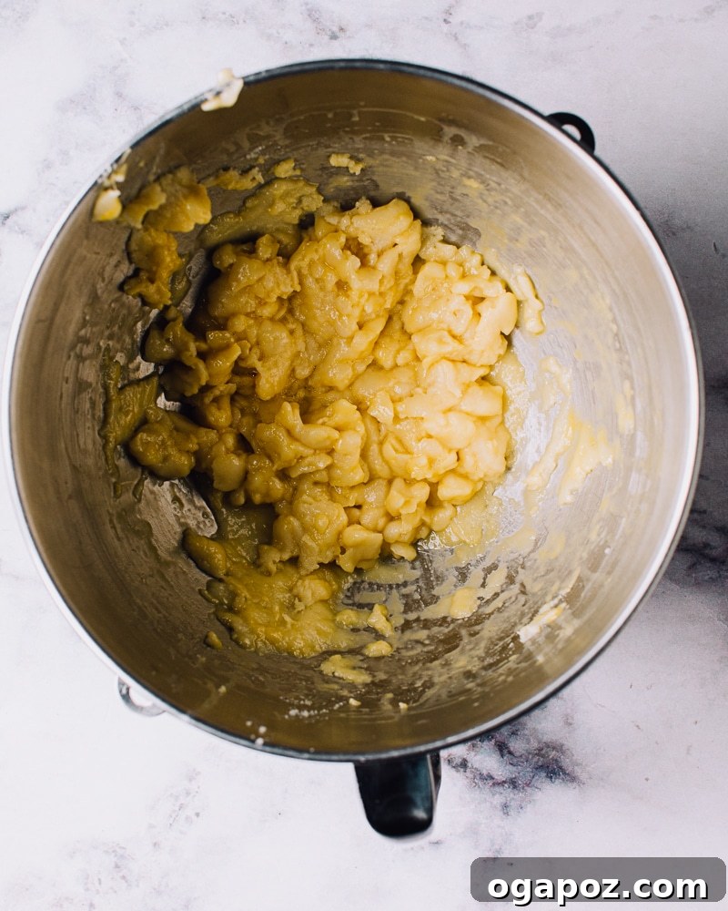 Airy French Delights 10 Beaten eggs being gradually incorporated into cooling choux pastry dough in a stand mixer.