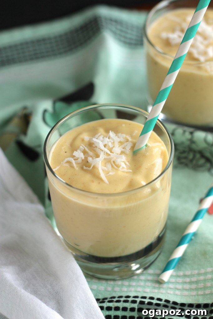 Tropical Mango Coconut Delight 4 Two glasses of Coconut Mango Smoothie, one with a straw, placed on a rustic wooden surface.