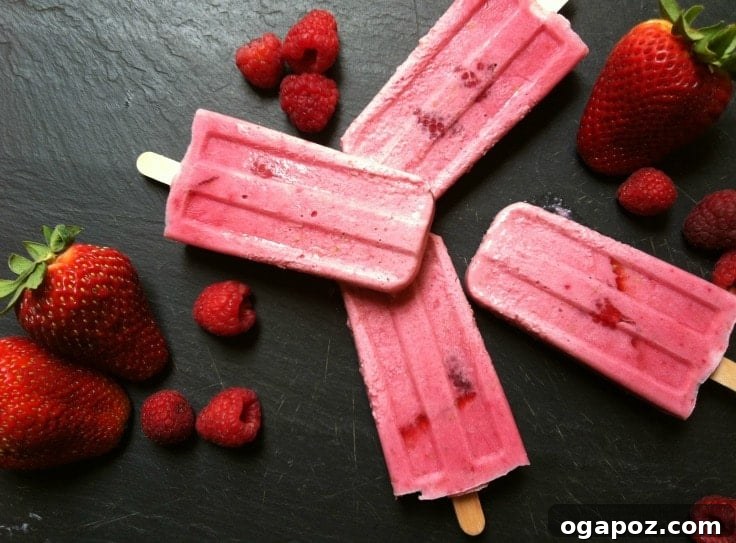 Strawberry Raspberry Dream Pops 3 An array of Strawberry Raspberry Cream Pops attractively displayed on a marble surface with fresh strawberries and raspberries as garnish.