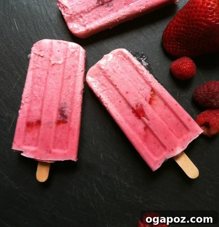 Strawberry Raspberry Dream Pops 4 A hand holding a vibrant Strawberry Raspberry Cream Pop against a blurred outdoor background, emphasizing its refreshing qualities.