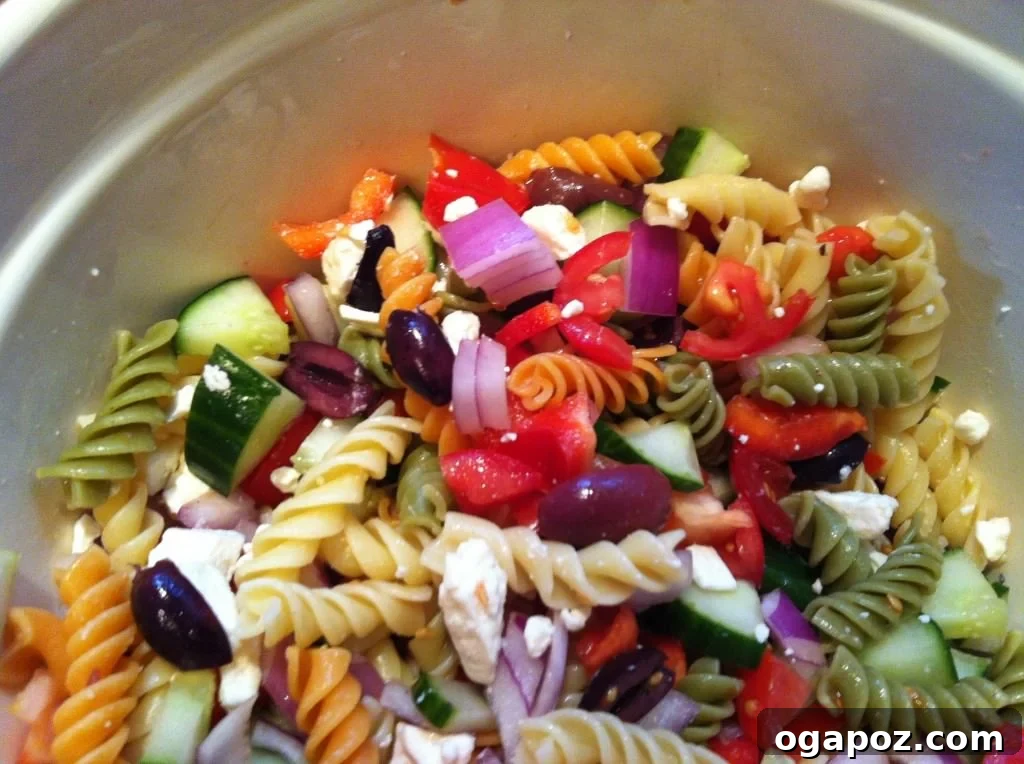 Vibrant Greek Pasta Medley 2 A colorful bowl of Greek Pasta Salad featuring tri-colored rotini pasta, chopped red bell peppers, cucumbers, cherry tomatoes, Kalamata olives, and crumbled feta cheese, garnished with fresh herbs.