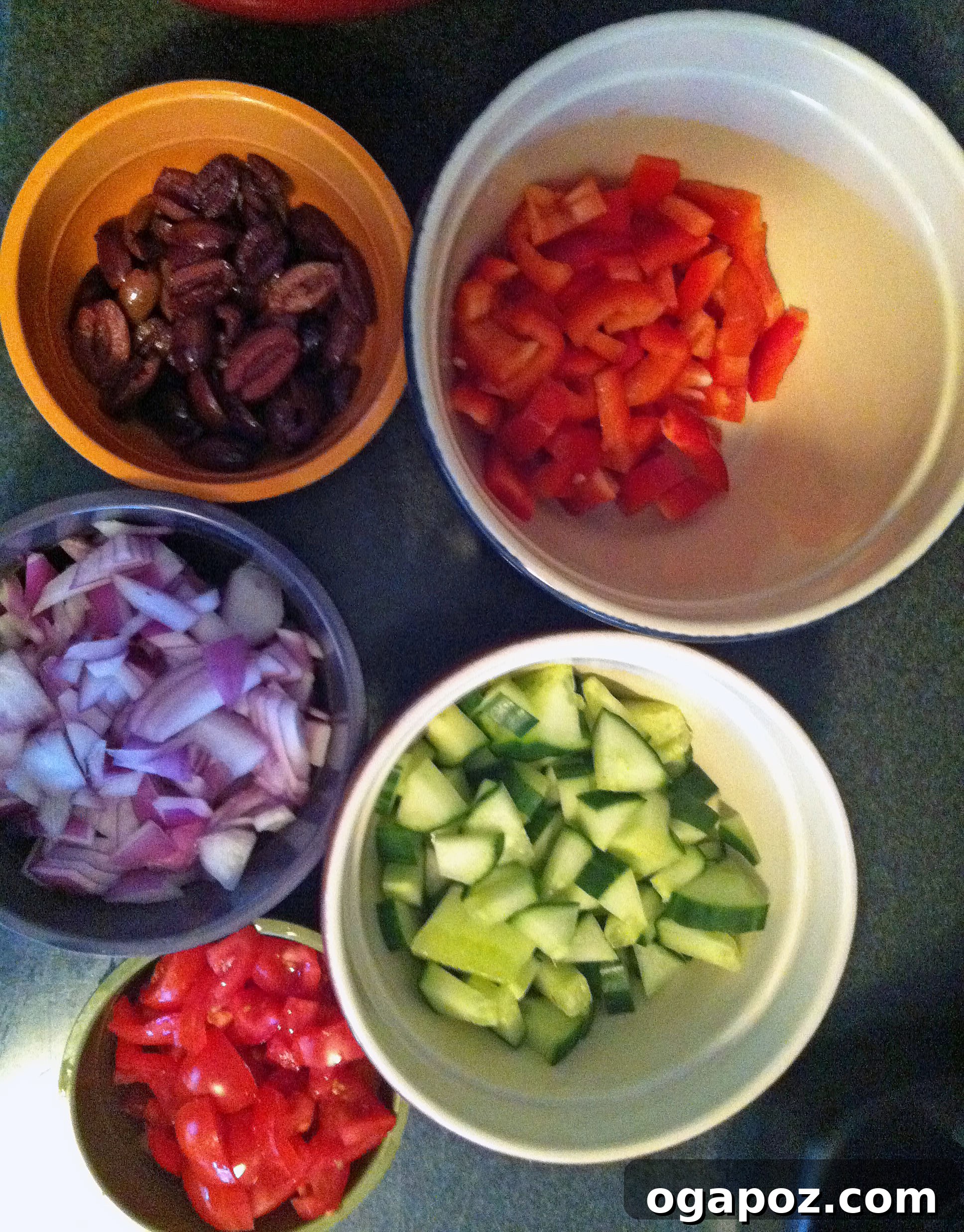Fresh, colorful vegetables and olives ready for our Greek Pasta Salad. A vibrant selection of fresh ingredients for Greek Pasta Salad, including a halved English cucumber, a red bell pepper, a small red onion, ripe cherry tomatoes, a bowl of Kalamata olives, and crumbled feta cheese.