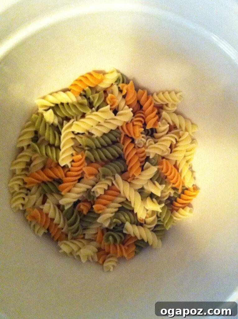 Tri-colored rotini pasta, a favorite for both kids and adults. A close-up shot of dry tri-colored rotini pasta, highlighting its fun curly shape and appealing mix of green, white, and orange colors.