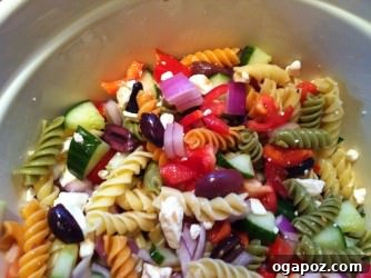 Mixed Greek Pasta Salad, ready for chilling. A large bowl filled with freshly tossed Greek Pasta Salad, showcasing the perfectly mixed pasta, vegetables, olives, and feta cheese, glistening with dressing.