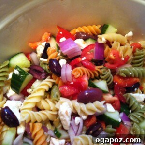 Vibrant Greek Pasta Medley 3 A close-up of the prepared Greek Pasta Salad in a white bowl, showing the intricate mix of pasta, colorful vegetables, feta, and olives, garnished with a sprig of fresh herb.