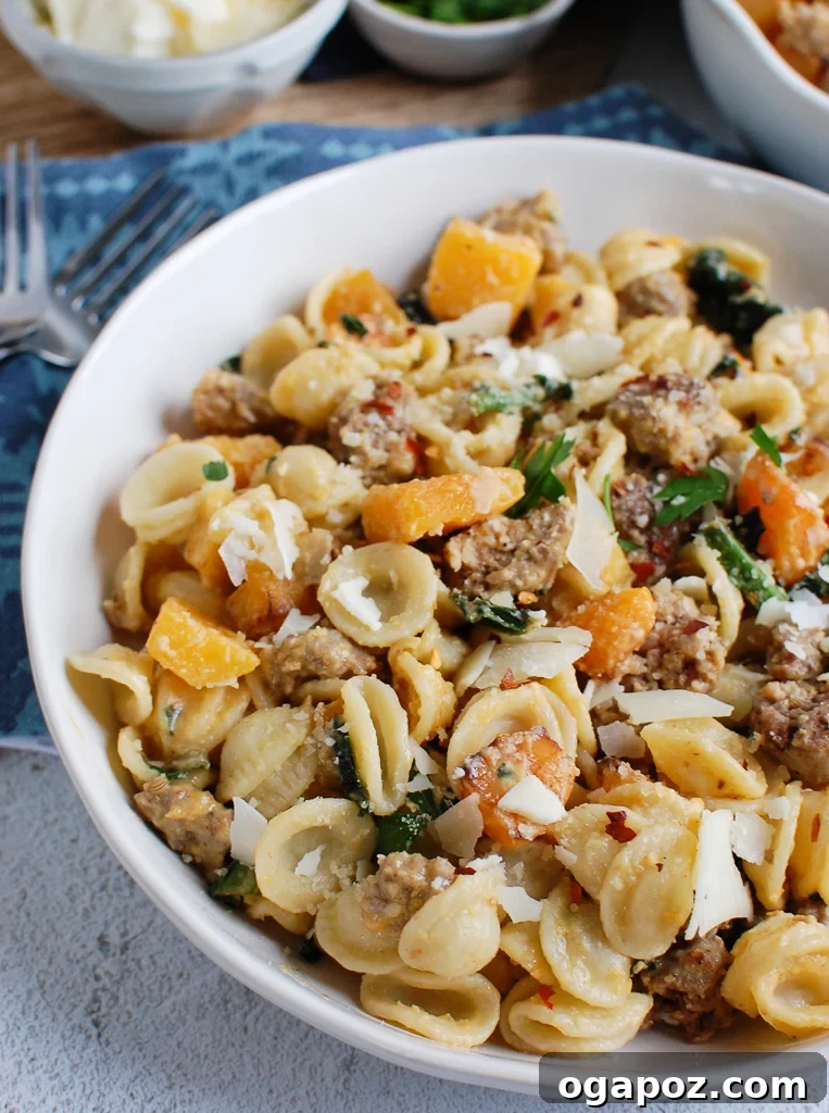 Golden Butternut Squash Pasta with Hearty Sausage 2 A vibrant bowl of butternut squash pasta, garnished with fresh sage and grated Parmesan cheese, invitingly served in a white ceramic bowl.