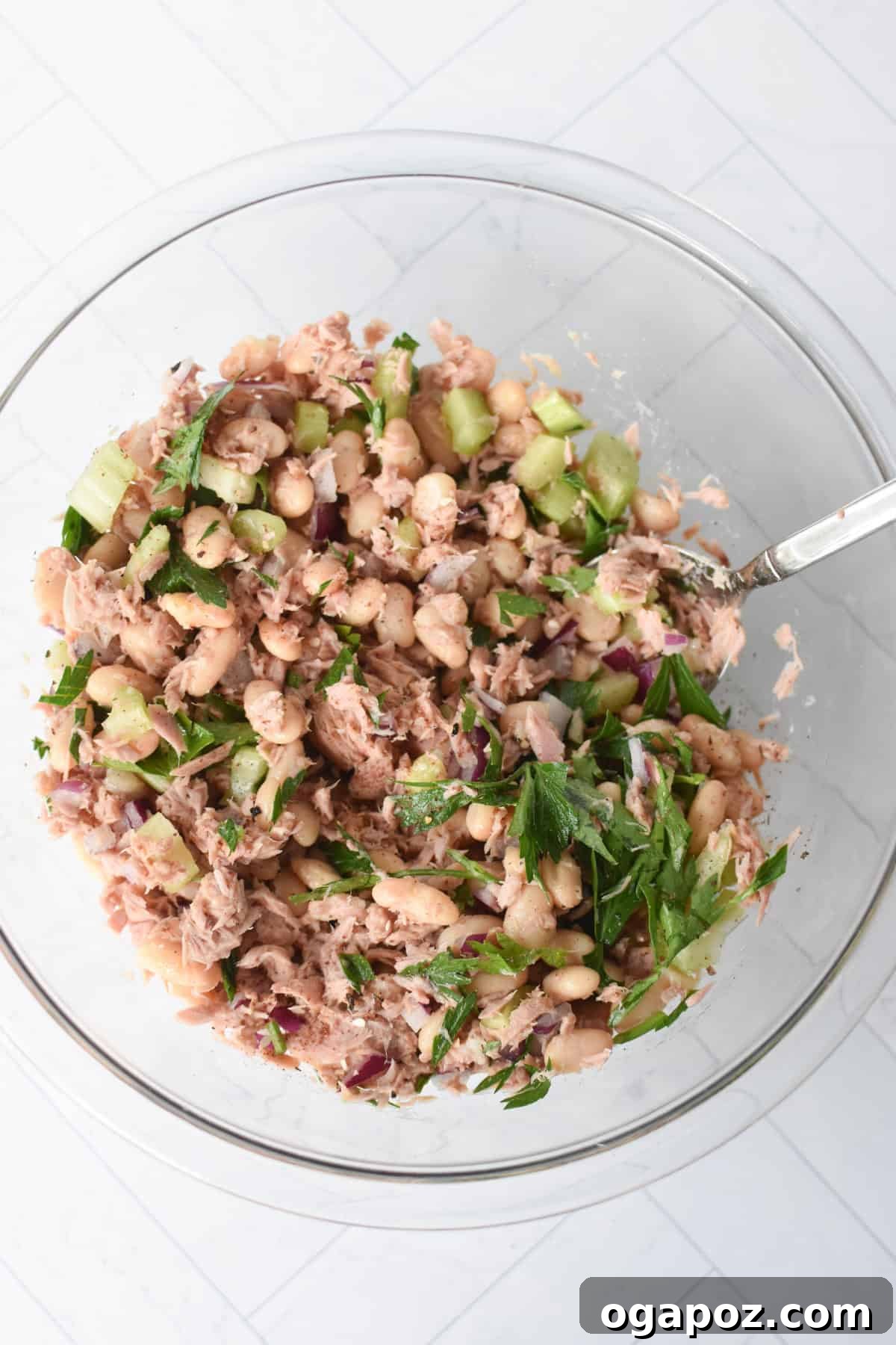 Tuna Bean Salad being dressed with lemon juice and olive oil in a clear bowl.