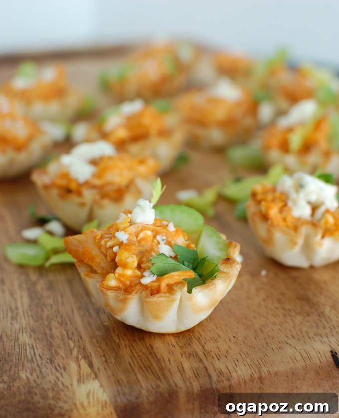 Tangy Buffalo Chicken Hummus Poppers 2 Crispy mini fillo shells filled with creamy, spicy buffalo chicken hummus, garnished with fresh celery and blue cheese crumbles.