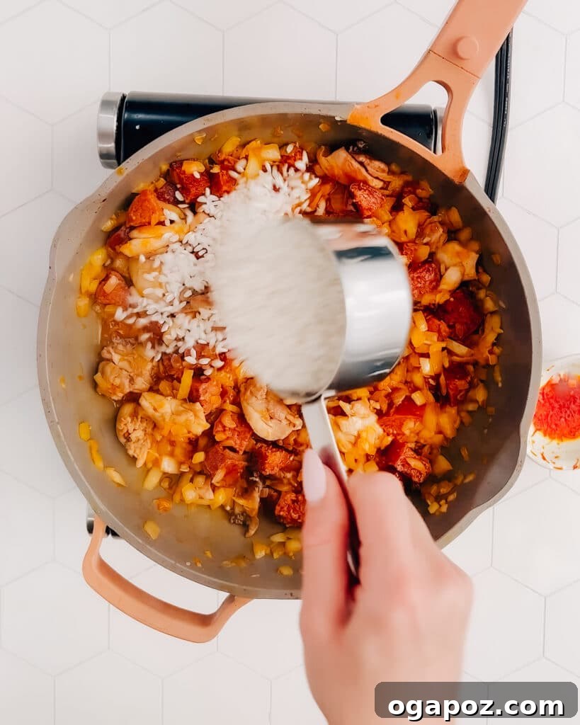 Spanish Surf and Turf Paella 4 Adding arborio rice to the seasoned liquid in a frying pan for paella.