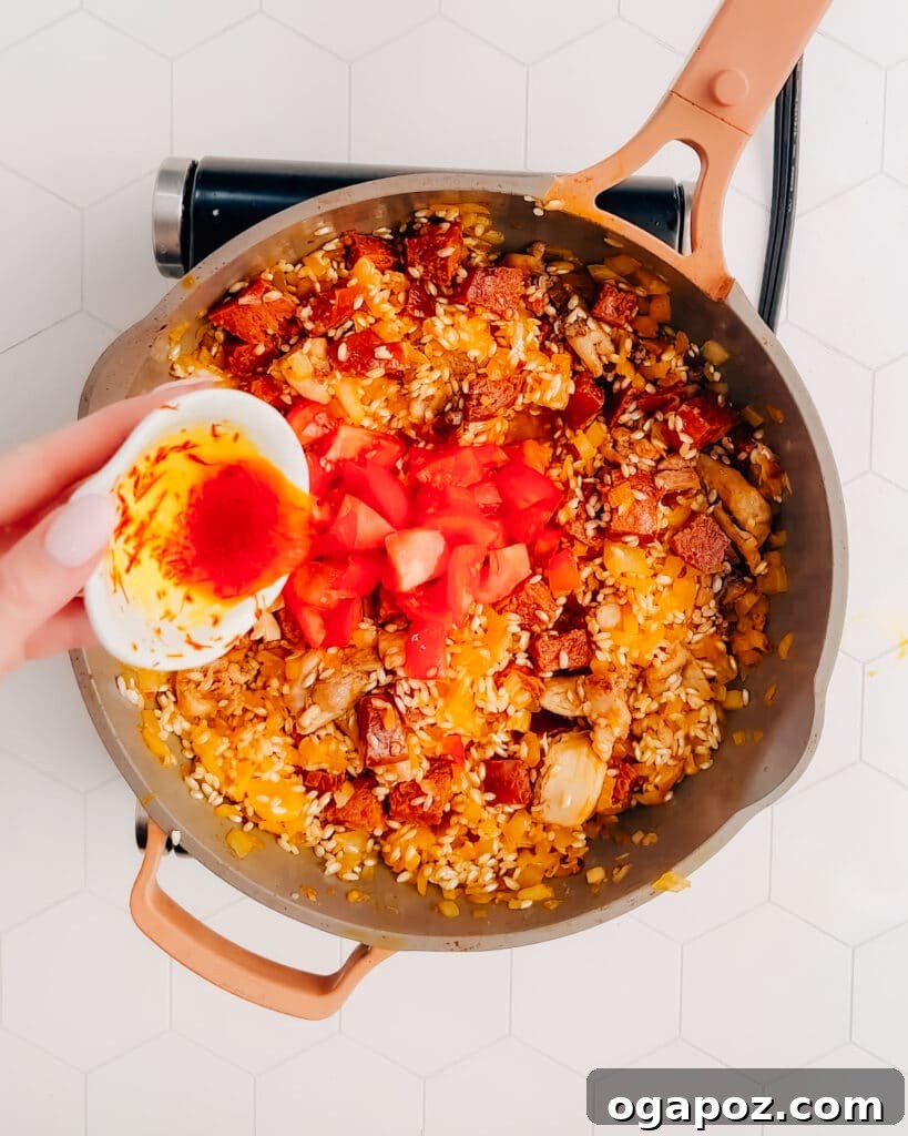 Spanish Surf and Turf Paella 5 Adding soaked saffron and diced tomatoes to paella in a frying pan for rich color and flavor.