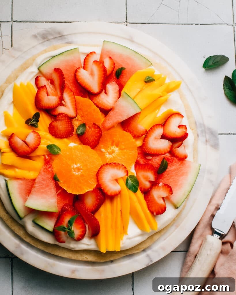 Ultimate Sugar Cookie Fruit Pizza 3 A close-up shot of an easy fruit pizza featuring a vibrant array of fresh fruits meticulously arranged on a fluffy cream cheese frosting and a golden sugar cookie base, ready for a spring or summer celebration.