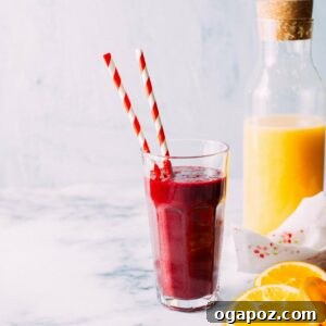 Vibrant Beet Berry Elixir 5 A glass of vibrant red smoothie with a fresh cherry garnish, next to a bowl of fresh cherries and an orange.
