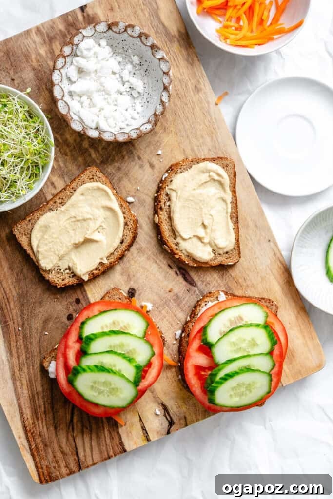 Layers of tomato and cucumber being added to bread with hummus.