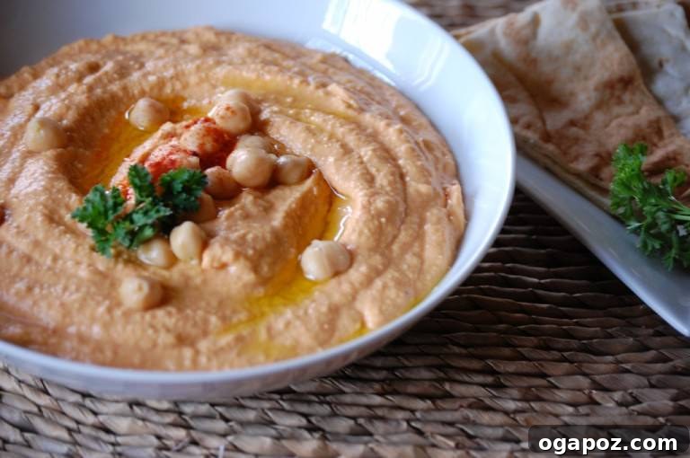 Beyond the Bowl: 12 Exciting Hummus Recipes 14 A rustic bowl of Roasted Red Pepper Hummus, garnished with sliced red peppers and olive oil.