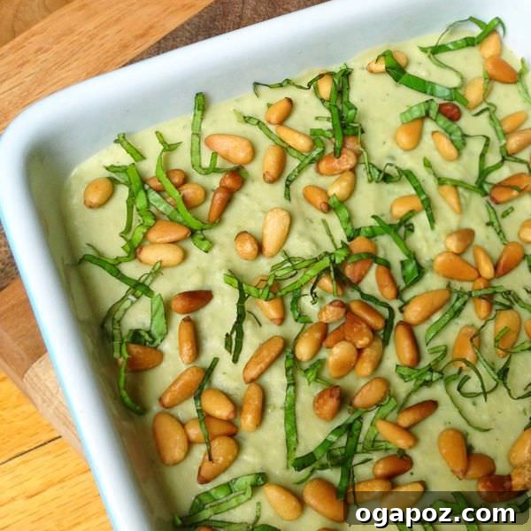 Beyond the Bowl: 12 Exciting Hummus Recipes 7 A charming bowl of Basil Pesto Hummus with Toasted Pine Nuts, adorned with fresh basil leaves.