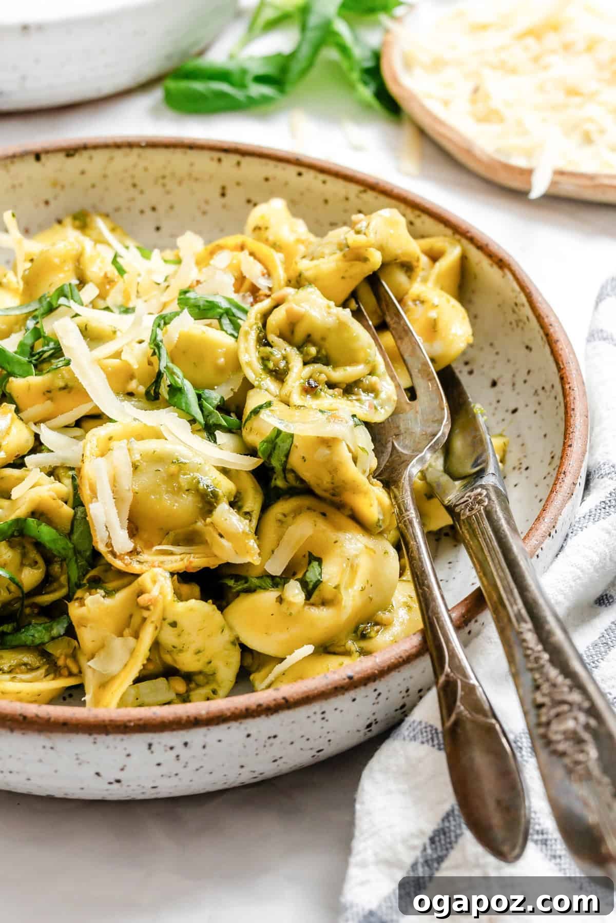 A bowl of creamy pesto tortellini with fresh basil and a fork resting on the side, ready to be enjoyed.