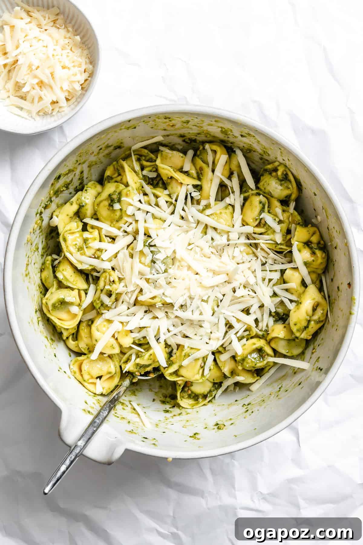 A large mixing bowl containing tortellini generously coated in vibrant green pesto and mixed with grated Parmesan cheese.