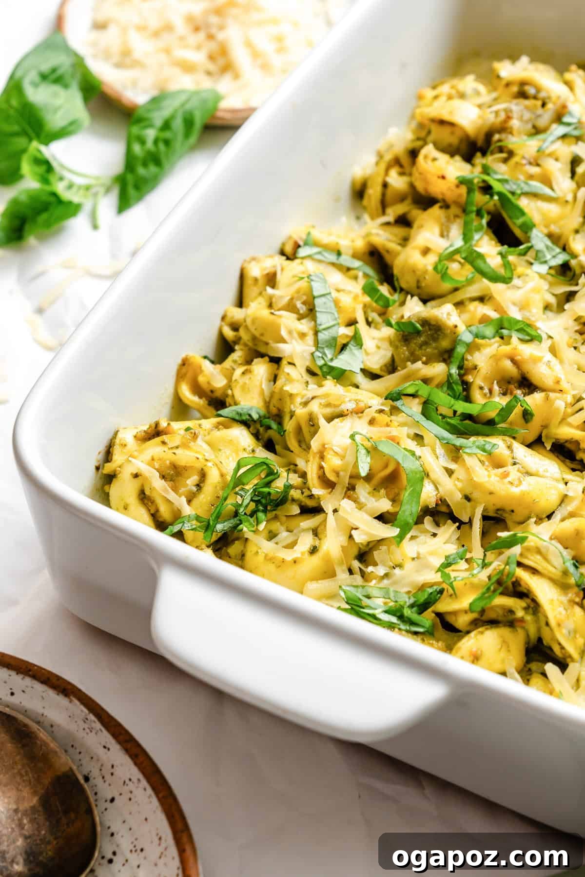 A close-up of the finished pesto tortellini dish, showing the melted golden cheese, vibrant green pesto, and fresh basil leaves.