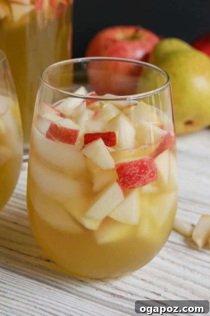 Bubbly Apple Pear Sangria 2 A tall glass filled with sparkling apple pear sangria, garnished with fresh apple and pear slices, on a rustic fall-themed background.