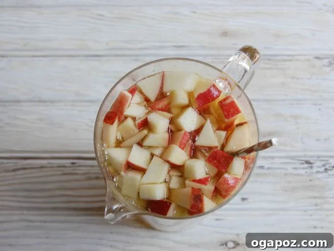 Bubbly Apple Pear Sangria 3 Close-up of sparkling apple pear sangria in a glass, with a focus on the bubbles and fruit slices, reflecting the warm autumn light.