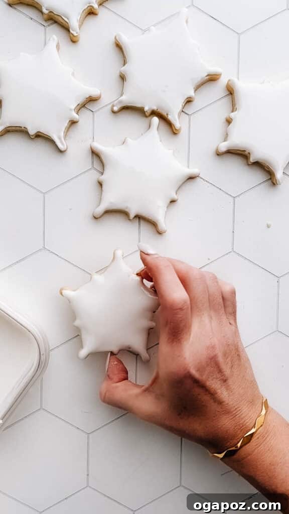 Sugar Snowflakes 10 Hand gently shaking a freshly iced snowflake cookie on the counter to level the royal icing surface.