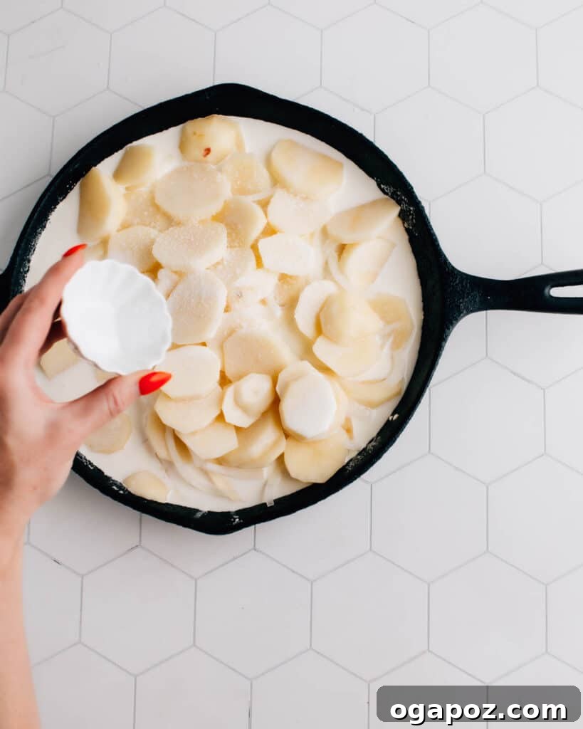 Comforting Gluten-Free Au Gratin Potatoes 4 Layered potatoes and onions in a skillet, with heavy cream being poured over them before seasoning.