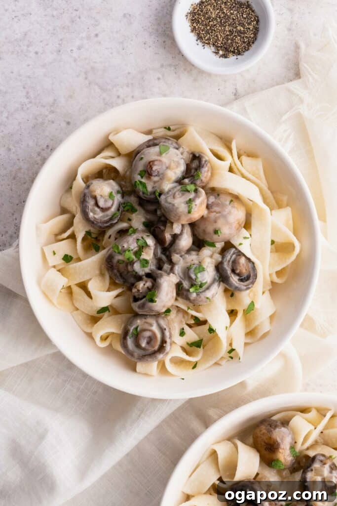 Wild Mushroom Pappardelle 8 Creamy Mushroom Pappardelle plated in a white bowl over a white cloth, accompanied by a small bowl of black pepper on the side.