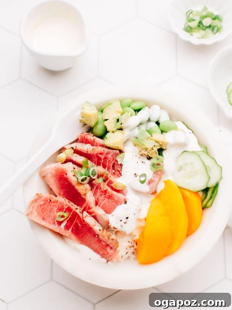 Flawless Air Fryer Tuna Steaks 2 A delicious air-fried tuna steak is served over a bed of rice, topped with dressing, cucumber, edamame beans, and sliced mango. A white spoon rests on the bowl, and small bowls of spring onions are placed nearby.