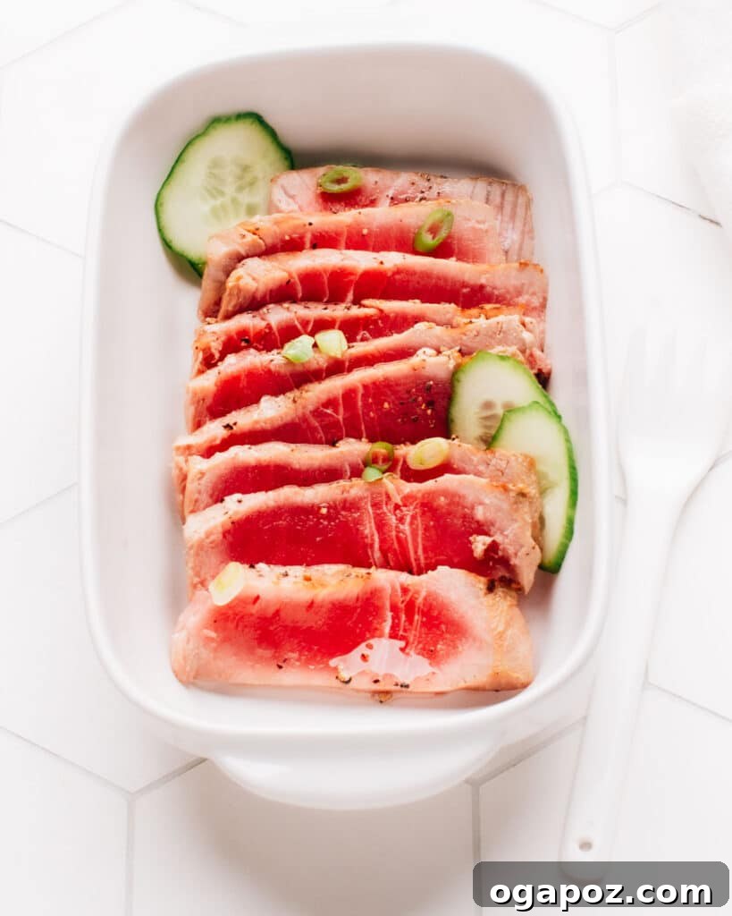 Flawless Air Fryer Tuna Steaks 5 Spring onions and cucumber slices top sliced air-fried tuna steak on a rectangular dish.