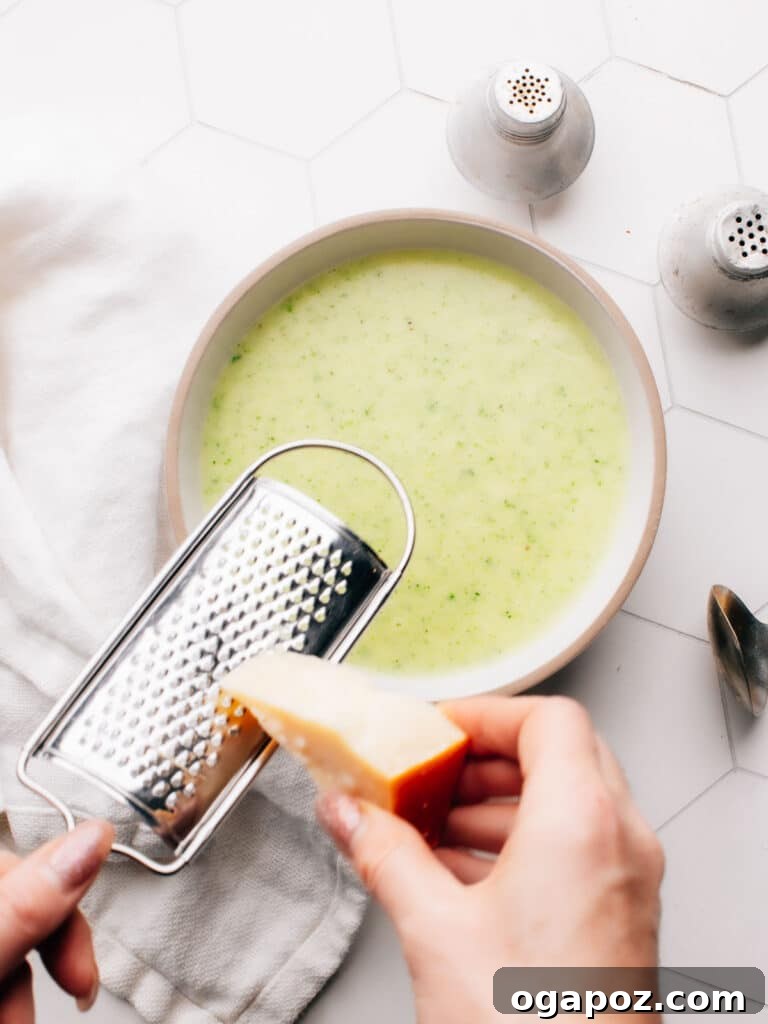 Velvety Potato Zucchini Puree 5 A hand grating fresh Parmesan cheese over a steaming bowl of potato zucchini soup.