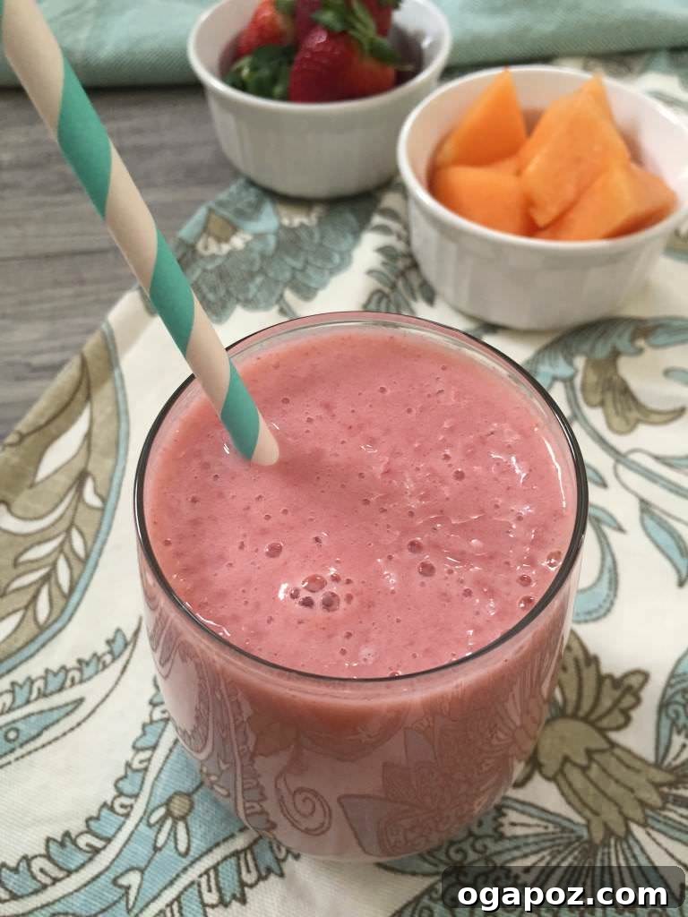 Bright and colorful Strawberry Cantaloupe Smoothie in a glass, garnished with fruit