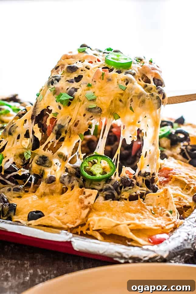 15 Easy Game Day Nachos Crowd Favorites 6 Person taking a heaping serving of two-bean vegetarian nachos from a sheet pan