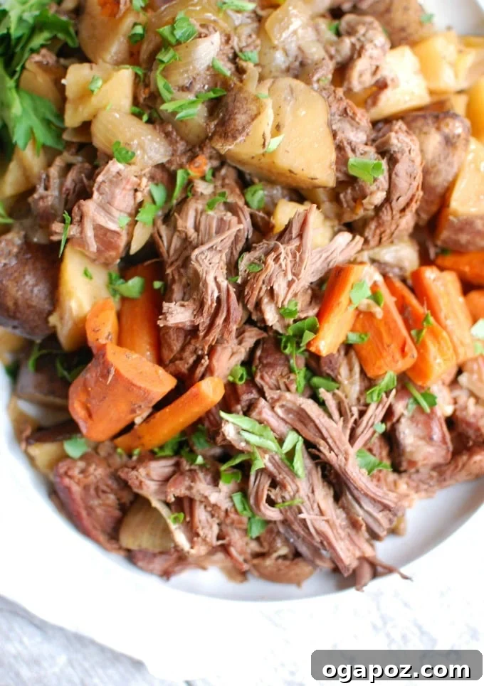 Succulent Crockpot Chuck Roast served on a white plate with gravy and fresh parsley garnish.