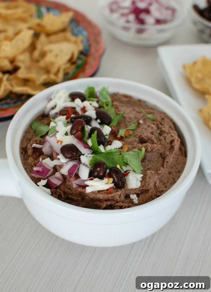 A bowl of creamy Black Bean Dip topped with crumbled Queso Fresco and fresh herbs, served with crispy tortilla chips, ideal for parties