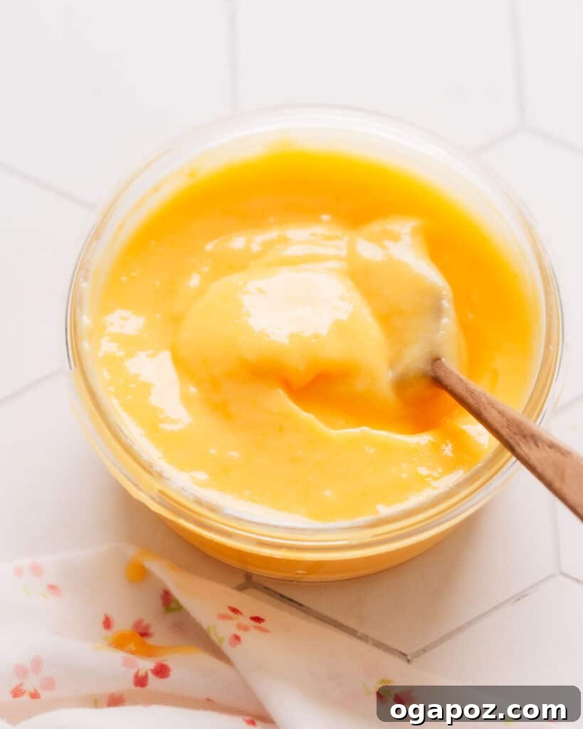 Zesty Lemon Curd Delight 6 A small glass cup holds fresh, creamy lemon curd, with a wooden spoon resting inside, ready to be used as a delicious filling.