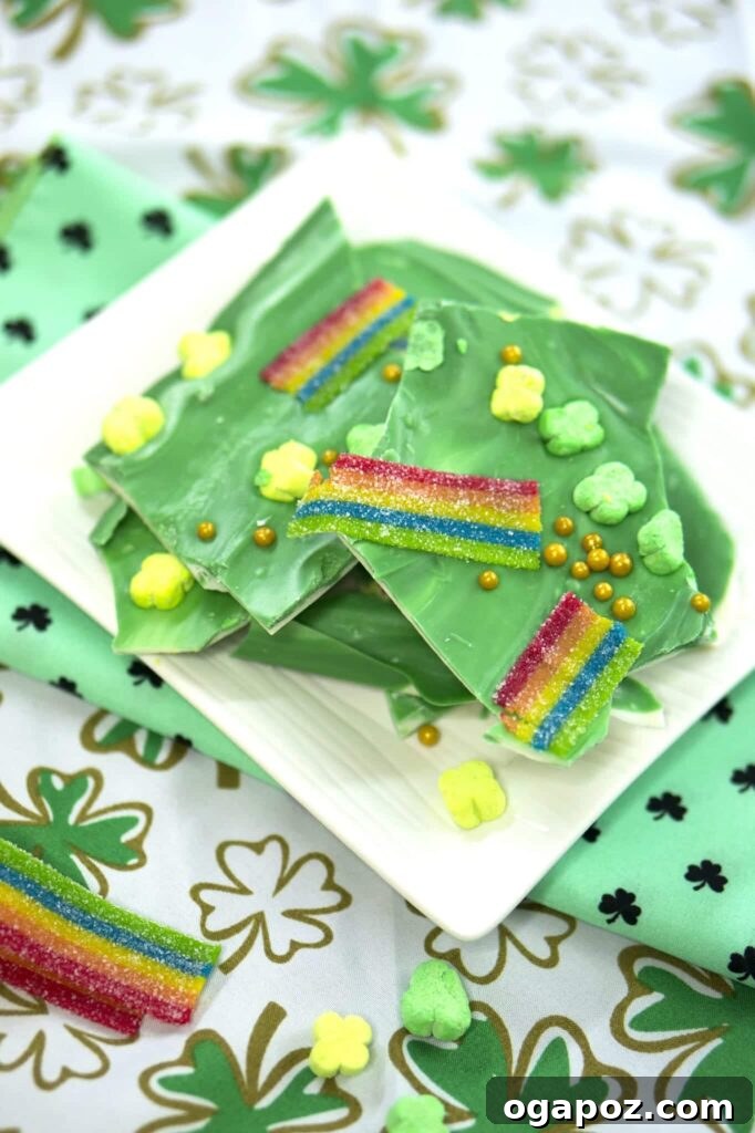 Luck of the Irish: Delicious Green Desserts for St Patricks Day 15 Stacked St. Patrick's Day leprechaun bark on a white plate. The bark is made of layers of chocolate and studded with festive sprinkles, gold dust, and shamrock-shaped candies, a vibrant green dessert.