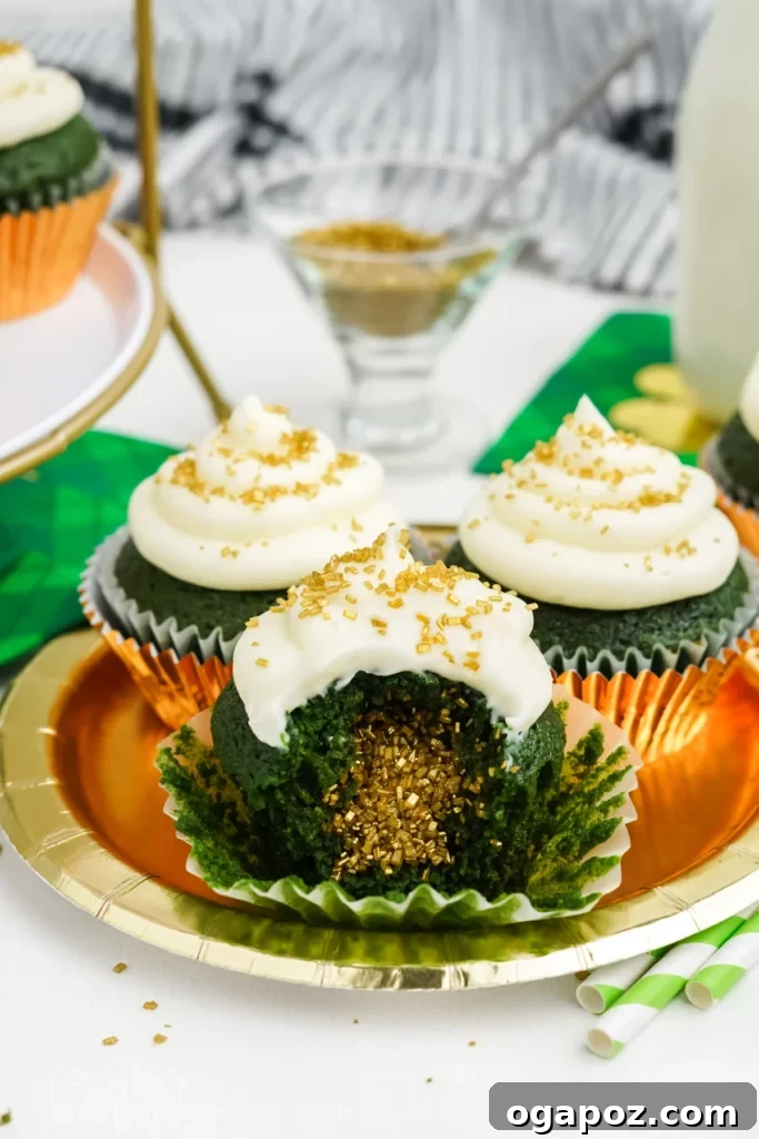 Luck of the Irish: Delicious Green Desserts for St Patricks Day 6 Three green velvet cupcakes with cream cheese frosting, placed on a golden plate. One of the cupcakes is sliced open, revealing a moist, green crumb with gold sparkles inside, celebrating St. Patrick's Day.