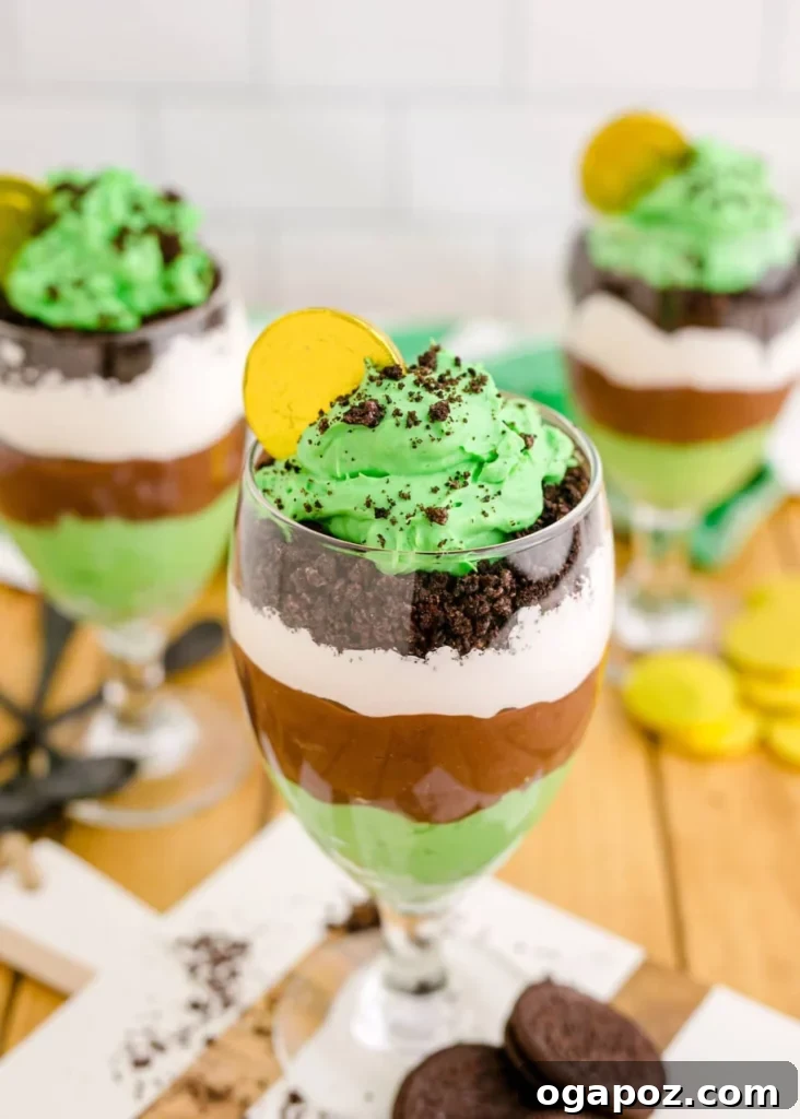 Luck of the Irish: Delicious Green Desserts for St Patricks Day 7 St. Patrick's Day Pudding Parfait, presented in a tall glass with a chocolate gold coin on top. The dessert consists of layers of creamy vanilla pudding and vibrant green pudding, creating a festive color scheme, ideal for celebrations.