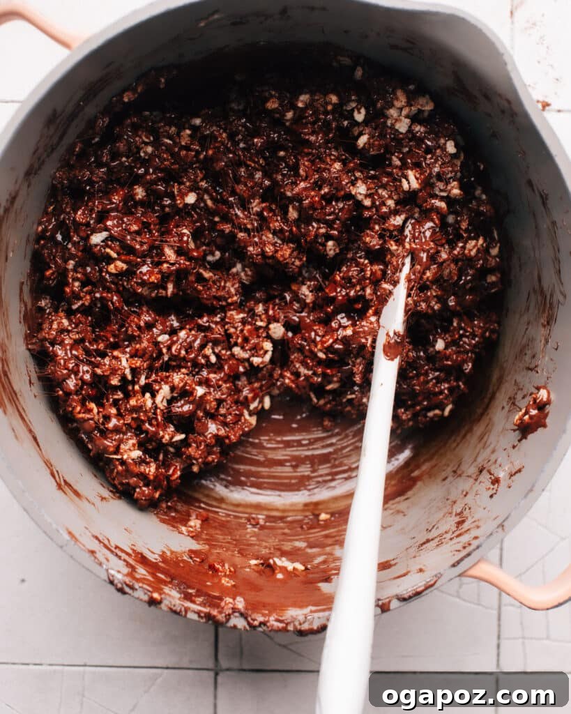 A saucepan filled with melted marshmallows, chocolate chips, and rice krispie cereal mixture ready to be poured into a baking sheet.