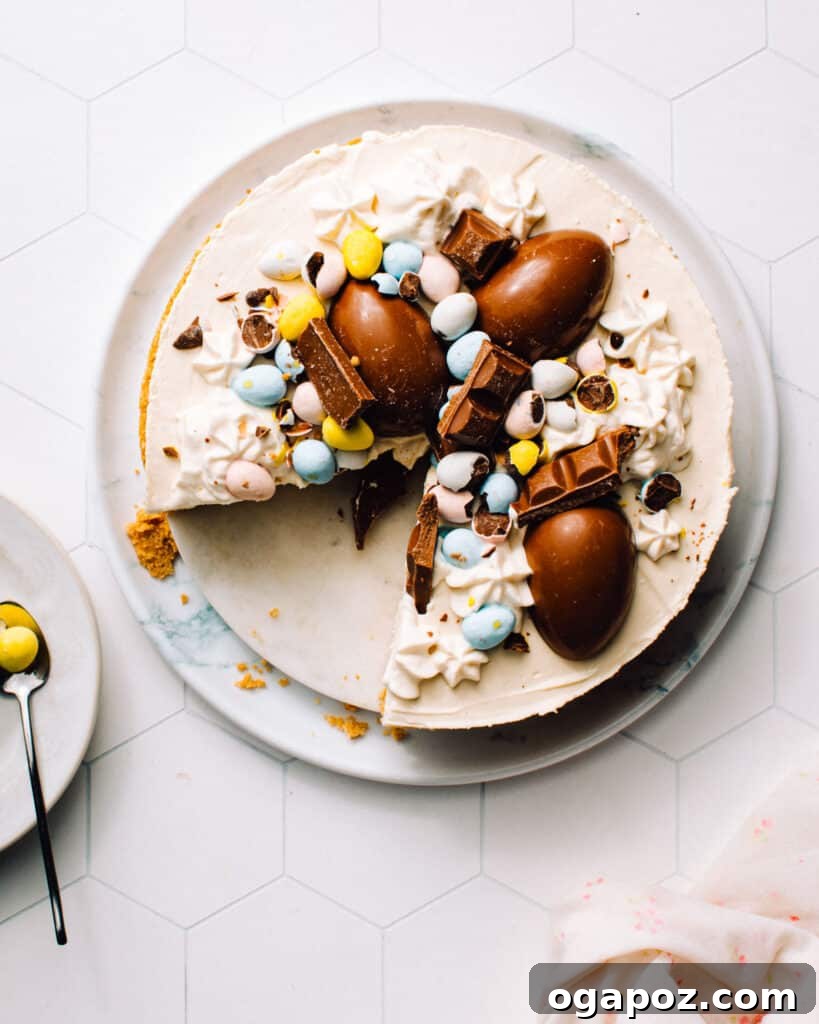 Colorful Easter Egg Cheesecake Chill 2 A beautifully decorated No-Bake Easter Egg Cheesecake on a large plate, adorned with colorful chocolate Easter eggs. A slice has been removed, showcasing its smooth, creamy filling and crunchy graham cracker crust.