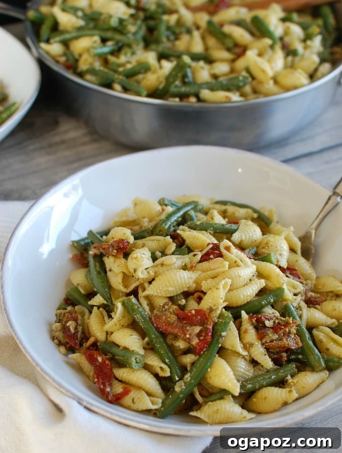 Sun-Drenched Pesto Pasta with Garden Beans and Tangy Tomatoes 2 Vibrant Pesto Pasta with Green Beans, Sun-dried Tomatoes, and Toasted Pine Nuts, garnished with fresh basil.