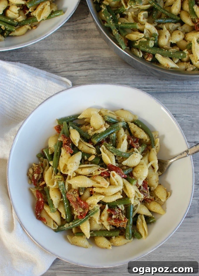 Sun-Drenched Pesto Pasta with Garden Beans and Tangy Tomatoes 3 Pesto Pasta dish with green beans, sun-dried tomatoes, and toasted pine nuts, presented on a plate with a napkin.