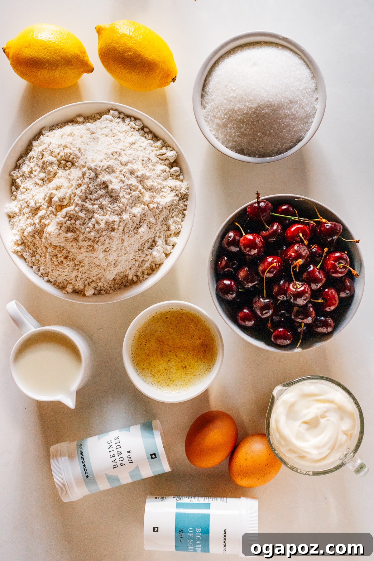 Bursting Cherry Muffins 3 A vibrant collection of fresh ingredients laid out, including flour, sugar, eggs, butter, sour cream, lemons, and a bowl of bright red sour cherries, ready for baking muffins.