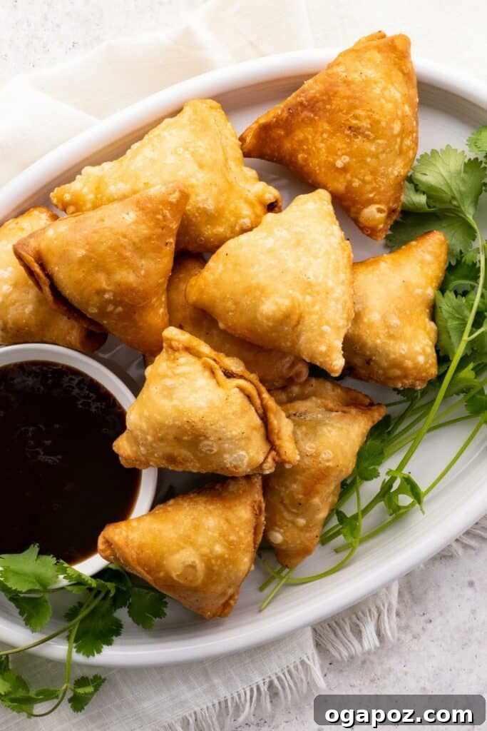 Flaky Spiced Potato Pockets 2 Crispy potato samosas served golden brown with a side of vibrant green chutney, hinting at their spicy, savory, and crunchy texture. Perfect as an appetizer or snack for any meal.