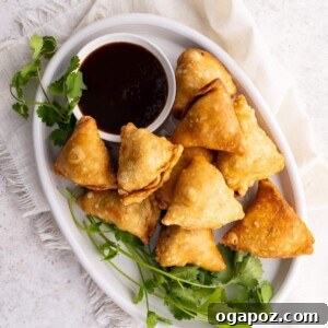A plate full of crispy potato samosas served with a side of chutney, showcasing their golden-brown and appealing texture.