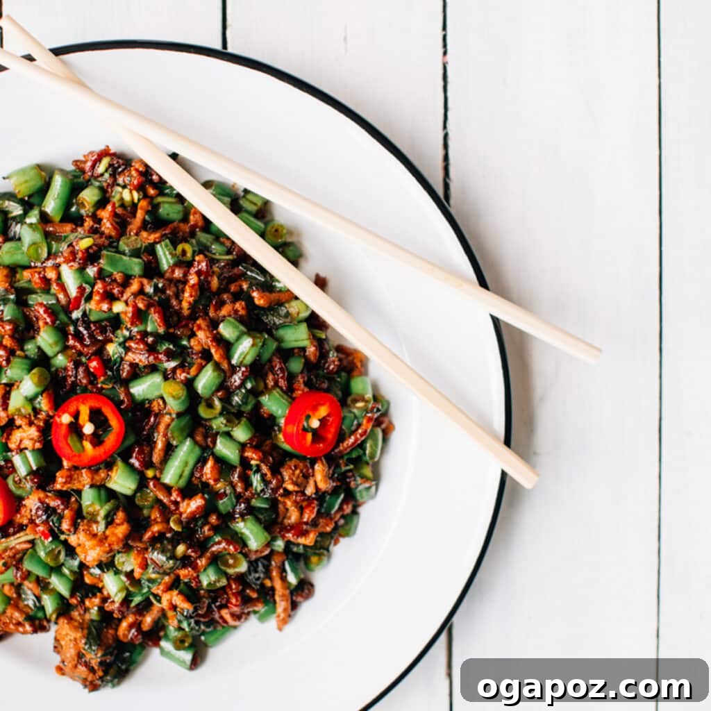 A beautifully plated dish of Thai Basil Pork with chopsticks, highlighting the vibrant green beans and rich brown sauce, ready to be eaten.