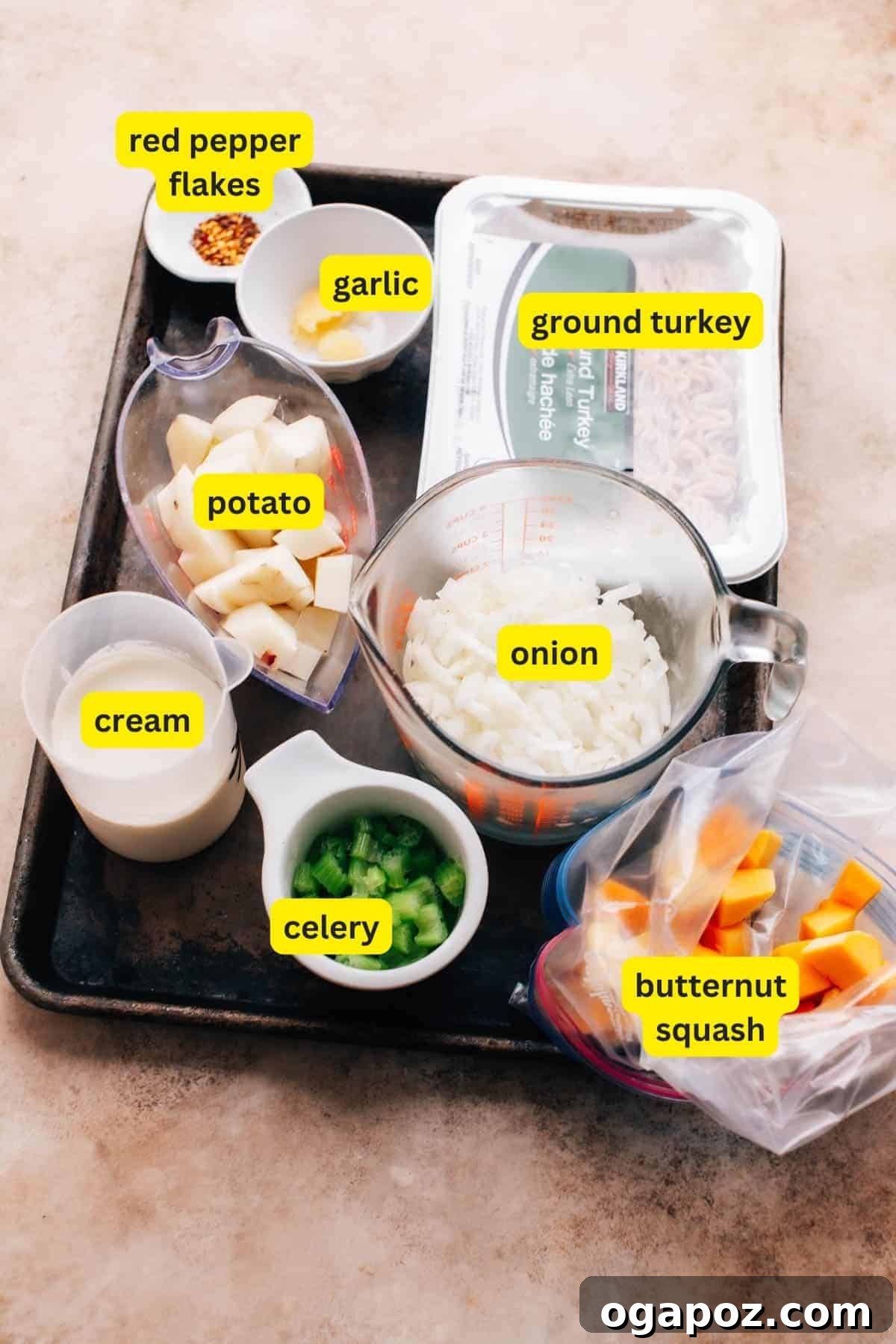 Hearty Turkey Mince Soup 3 A vibrant and carefully arranged collection of fresh ingredients destined for ground turkey soup, displayed appealingly on a clean kitchen countertop. The selection includes crisp chopped celery, lean raw ground turkey, finely diced onion, fragrant minced garlic, a small dish of fiery red pepper flakes, perfectly cubed potato, bright orange butternut squash chunks, and a small jug of rich cream. All elements are prepared and ready to begin the cooking process.