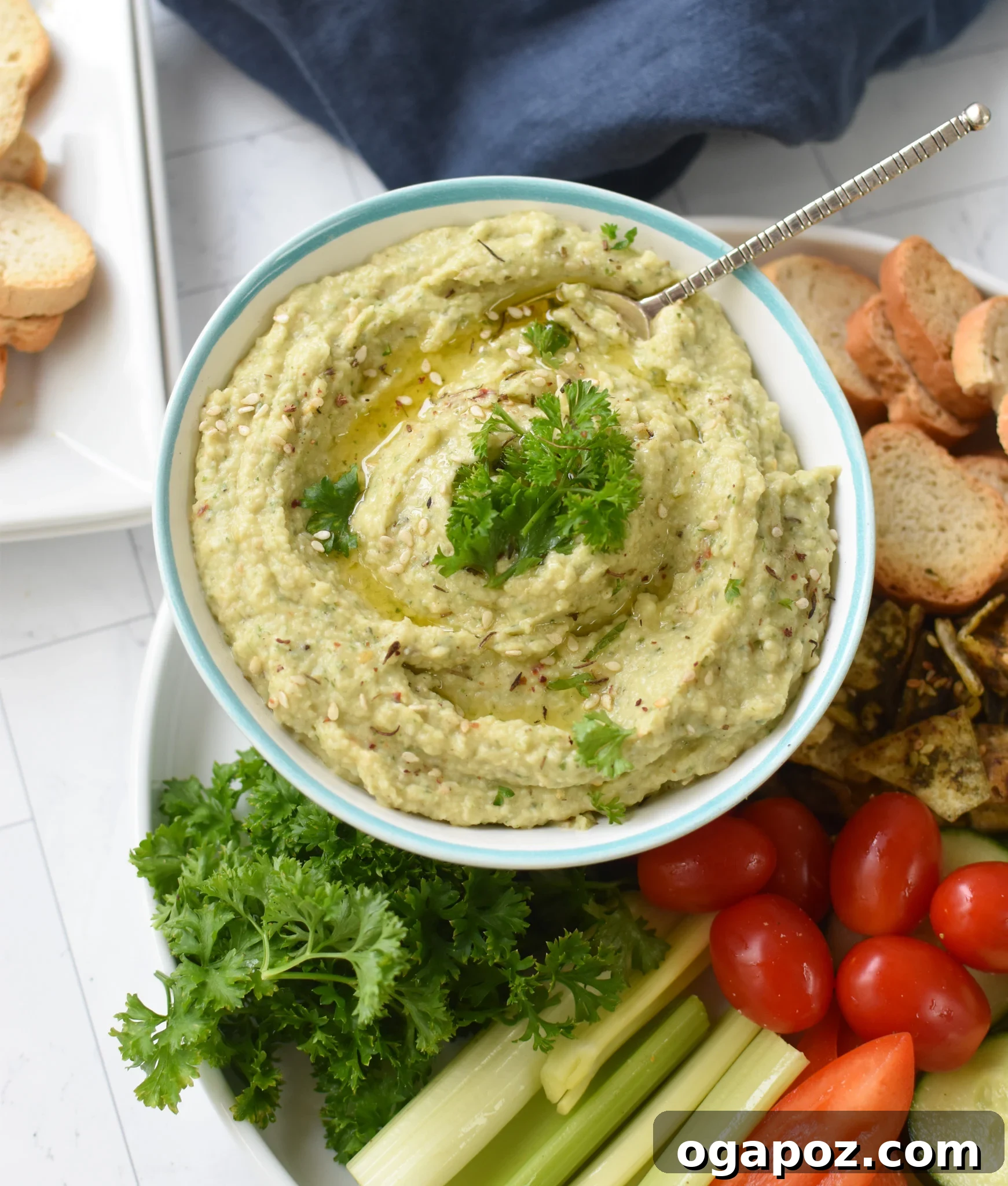 Creamy White Bean Artichoke Dip 3 A vibrant bowl of White Bean Artichoke Dip garnished with fresh herbs, surrounded by crostini and fresh vegetables, ready for dipping.